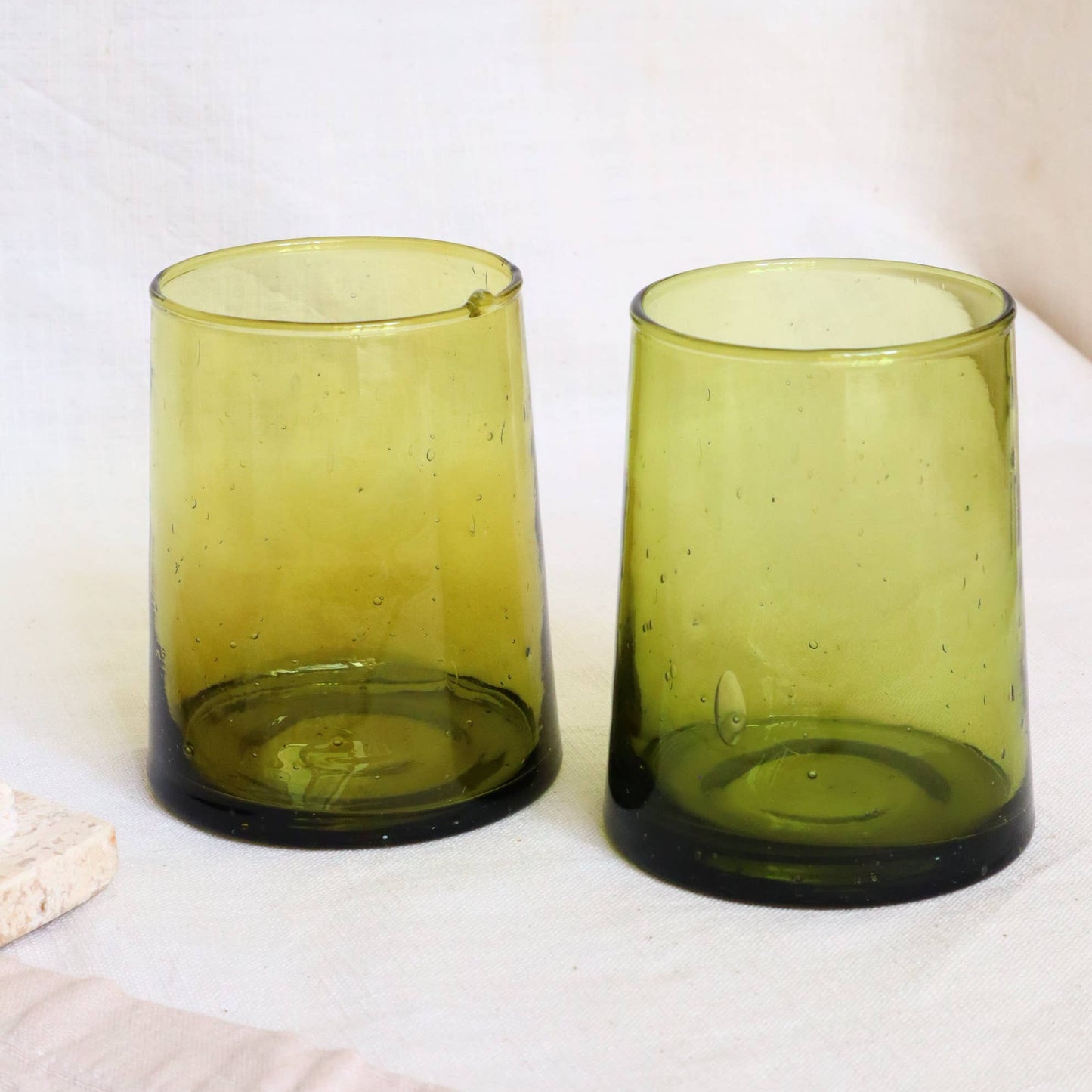 Two green glass tumblers on a light wooden surface with a white background