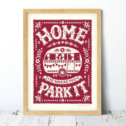A vintage inspired red and cream caravan print with the text 'Home is Where You Park It' and decorative floral elements.