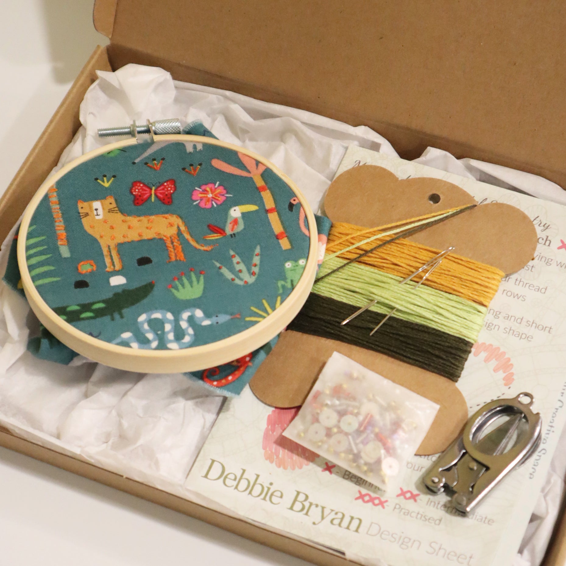 Embroidery kit with hoop, fabric, threads, and sewing materials in a box, featuring a jungle design on the fabric.