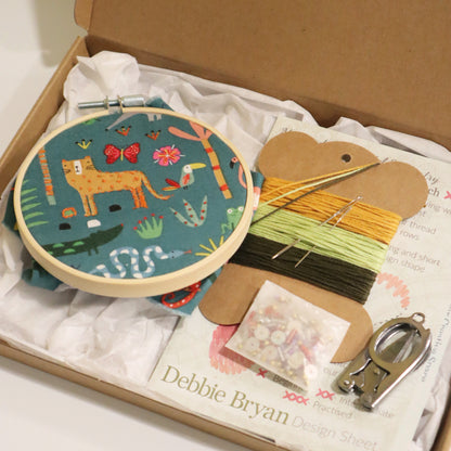 Embroidery kit with hoop, fabric, threads, and sewing materials in a box, featuring a jungle design on the fabric.