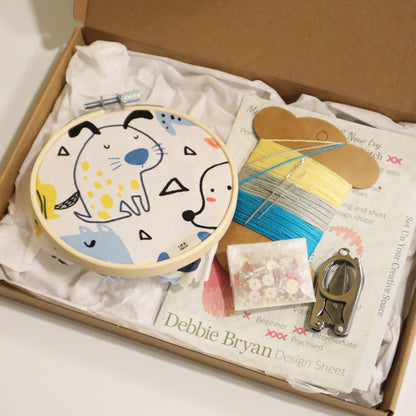 Embroidery hoop with a dog design, thread, and sewing materials in a box, featuring Debbie Bryan branding.