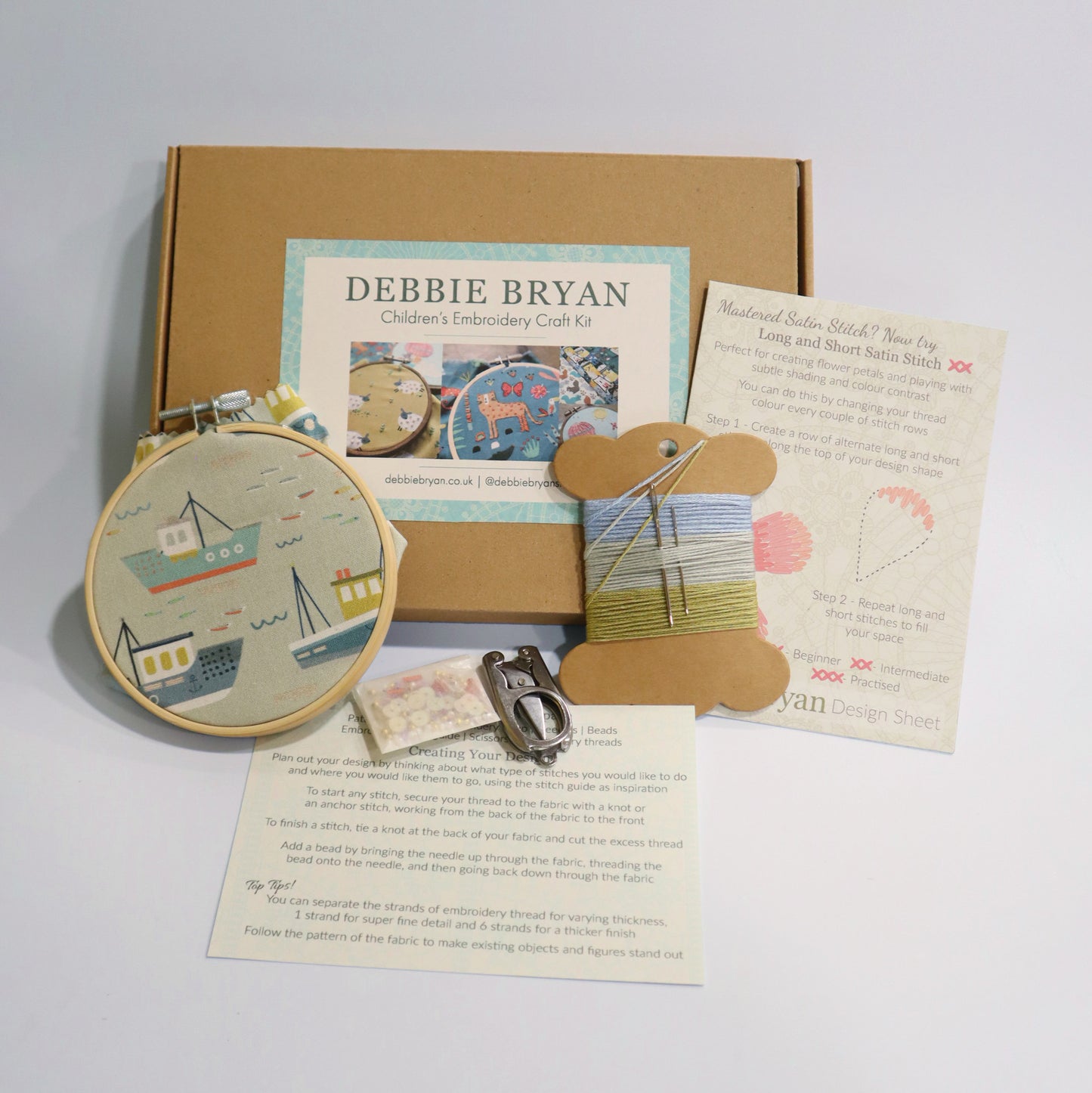Boat themed children's embroidery craft kit with hoop, thread, and instructions from Debbie Bryan on a light grey background.