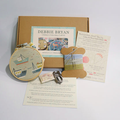 Boat themed children's embroidery craft kit with hoop, thread, and instructions from Debbie Bryan on a light grey background.