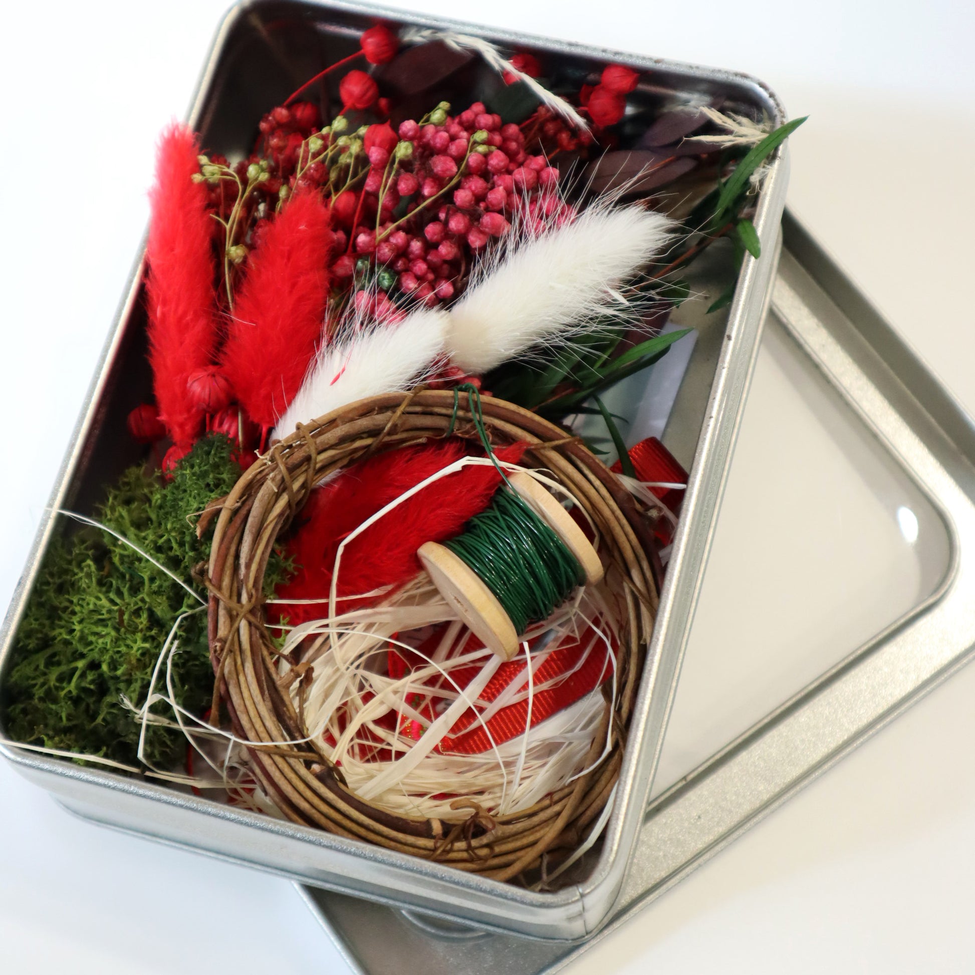 A small red and green dried flower bunch and a small vine vine wreath sat in a metal tin