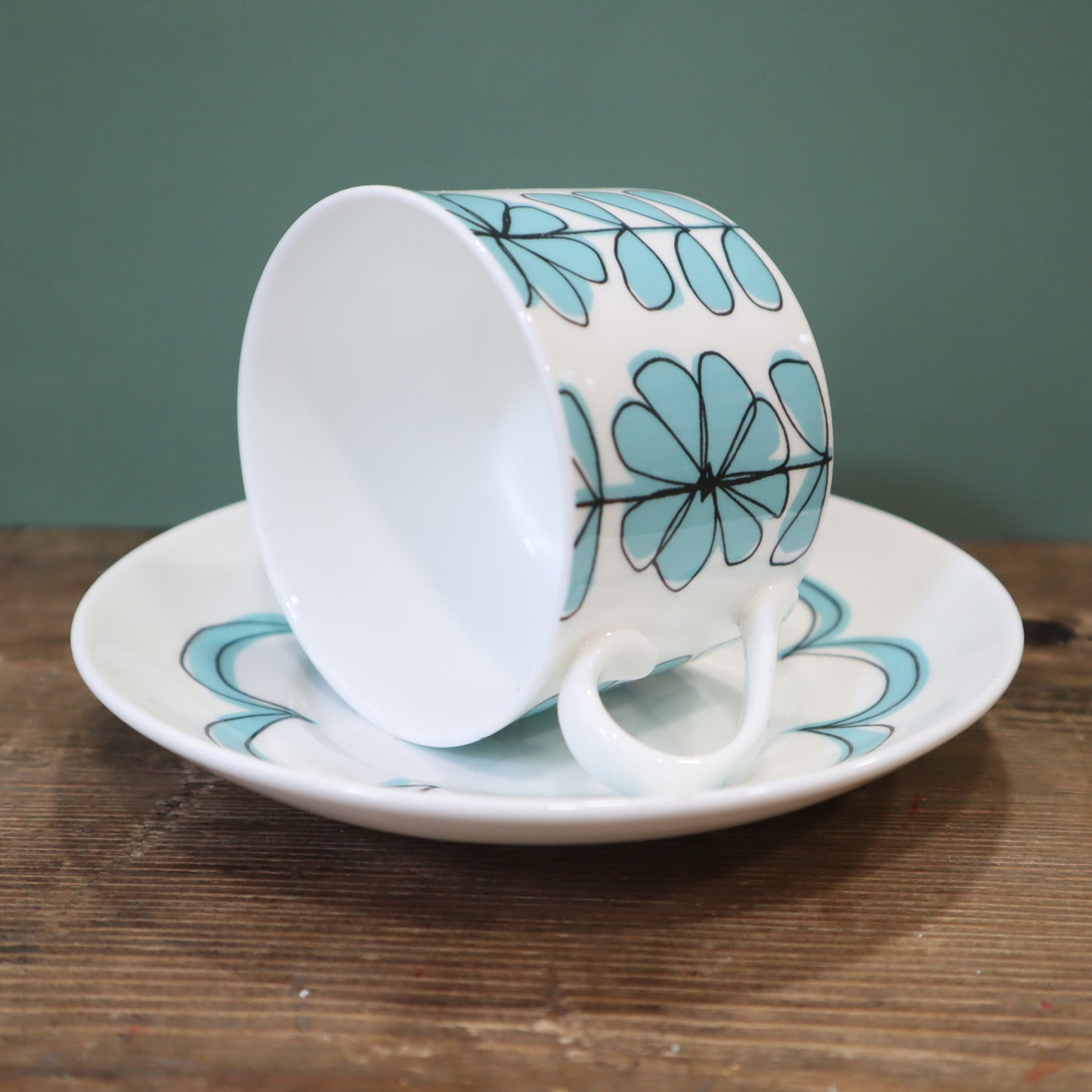 Ceramic cup and saucer with blue floral design on a wooden surface.