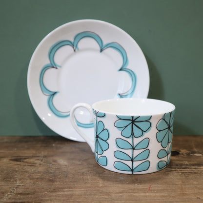 Ceramic cup and saucer with blue floral design on a wooden surface and green background