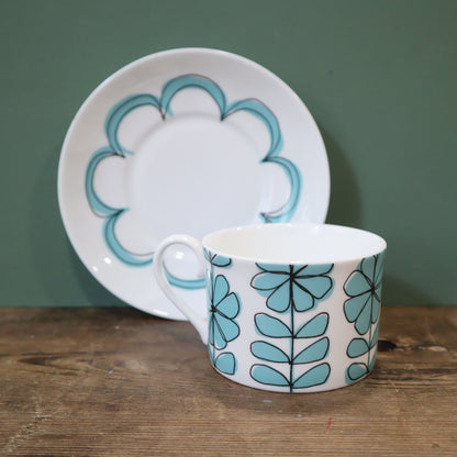 Ceramic cup and saucer with floral design on a wooden surface and green background