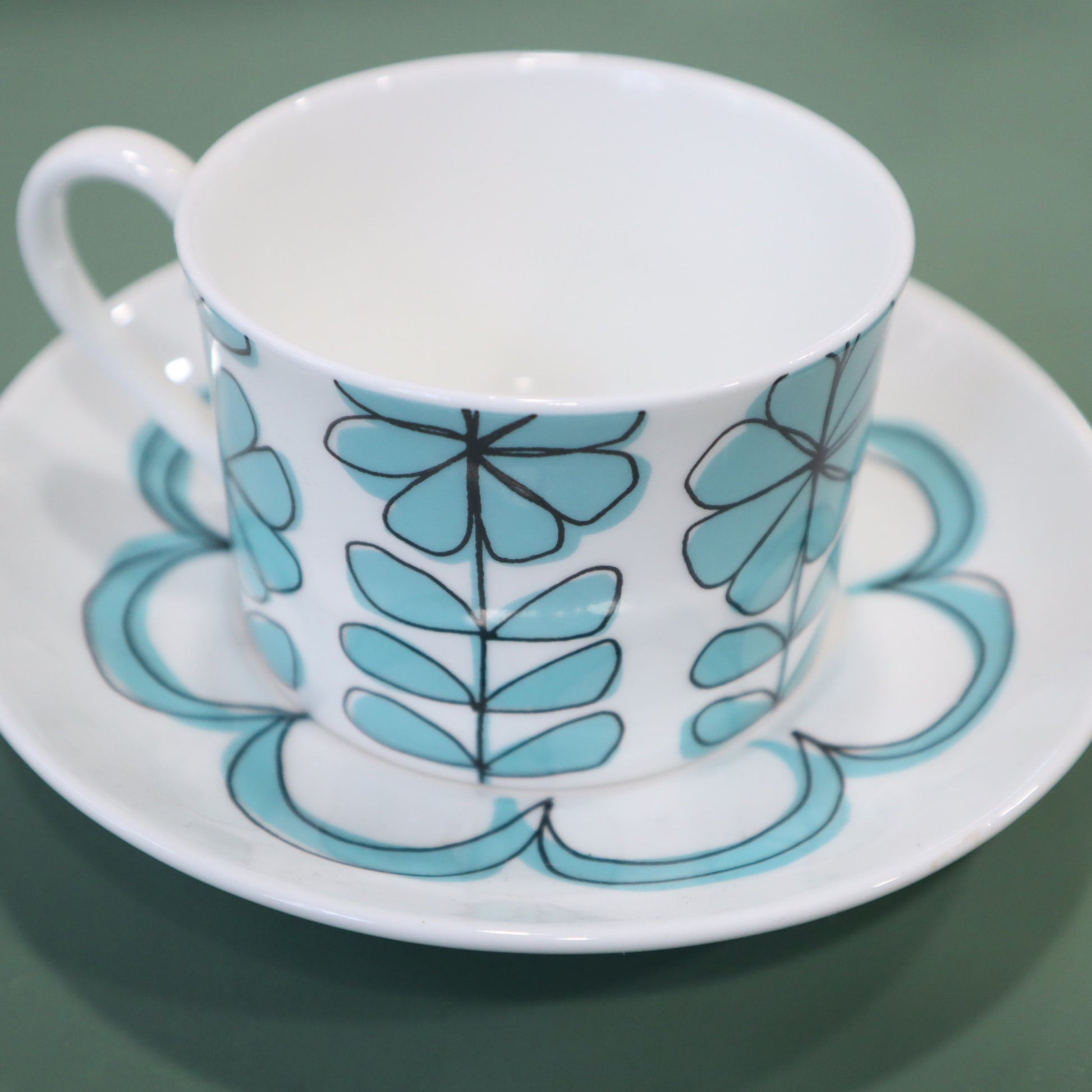 Ceramic cup and saucer with blue floral pattern on a green background