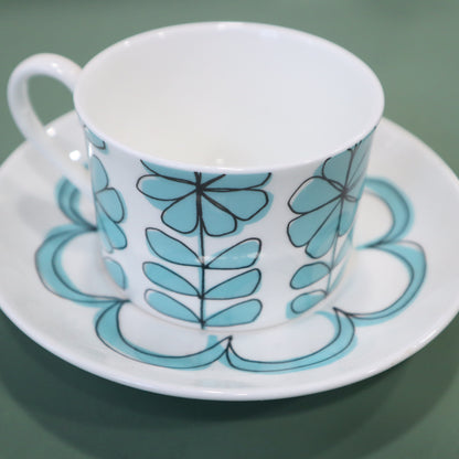 Ceramic cup and saucer with blue floral pattern on a green background