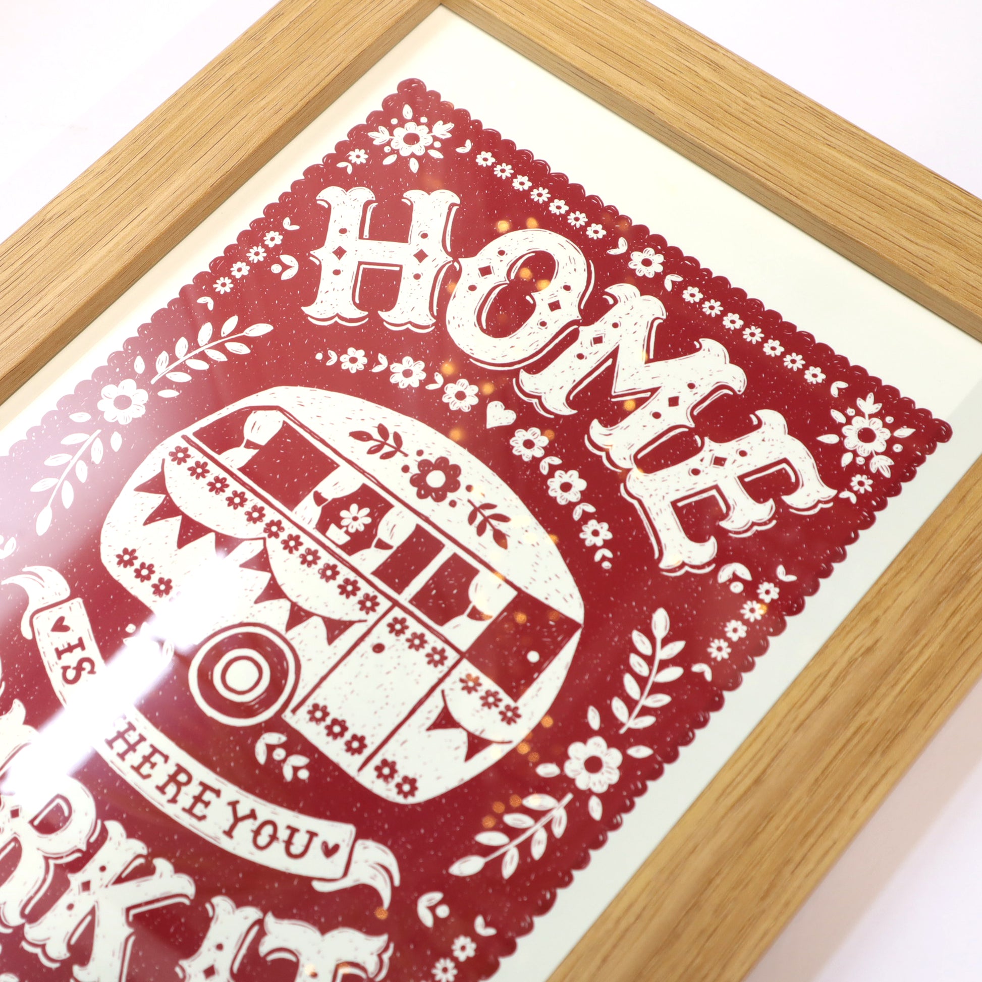 Decorative print with 'Home is where you park your camper' text on a red background, framed in wood.