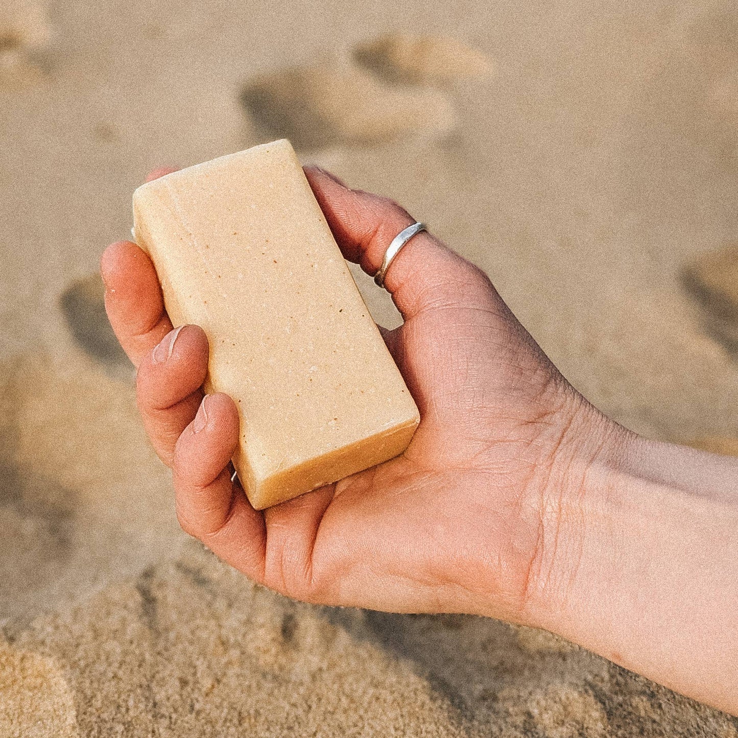 A hand holding a bar of soap on a sand background