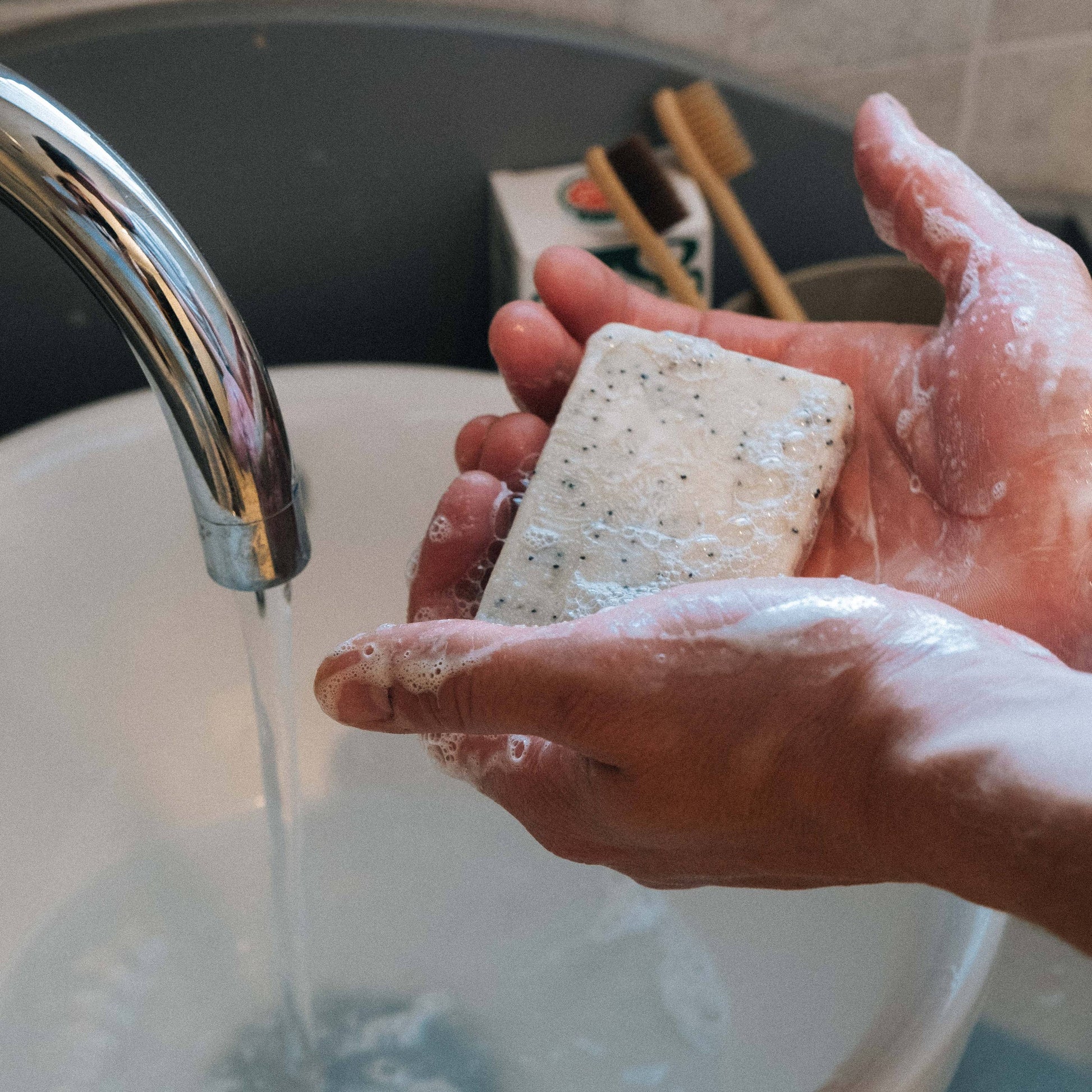 Someone washing their hands with a bar of soap under a silver tap