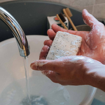 Someone washing their hands with a bar of soap under a silver tap