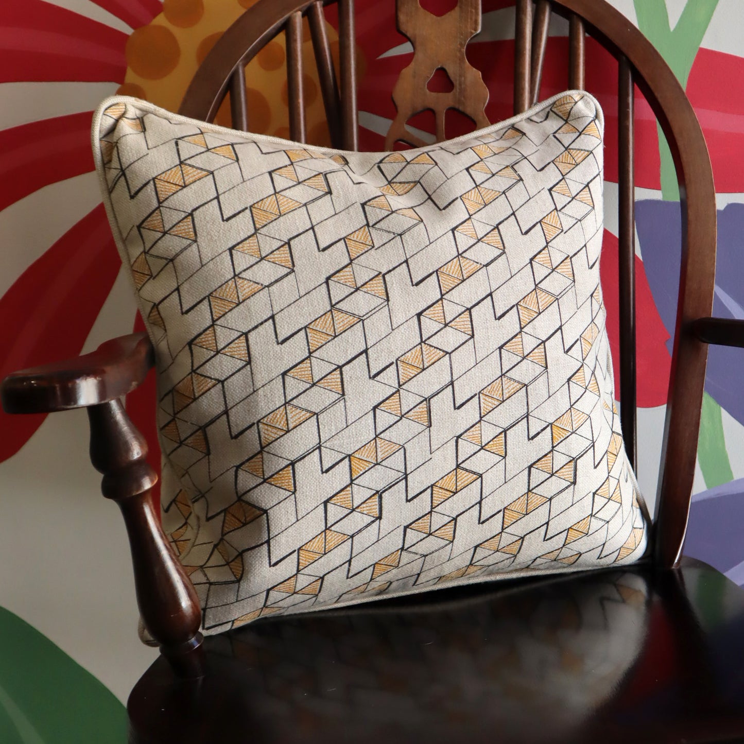 Decorative pillow with geometric pattern on a wooden chair against a colorful abstract background