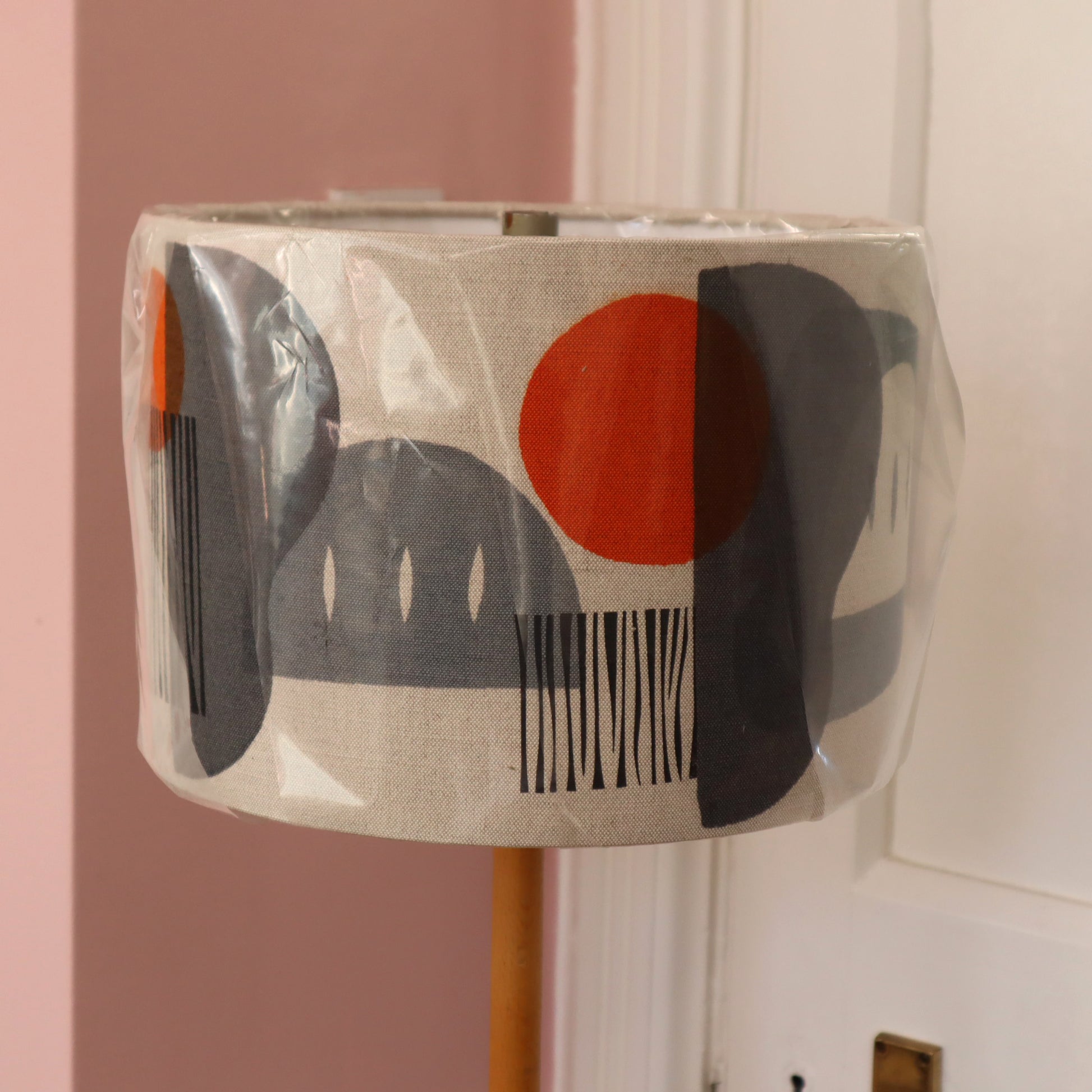 Decorative lampshade with abstract design in clear packaging against a pink wall.