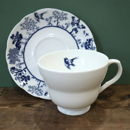 White teacup and saucer with blue floral and bird design on a wooden surface.