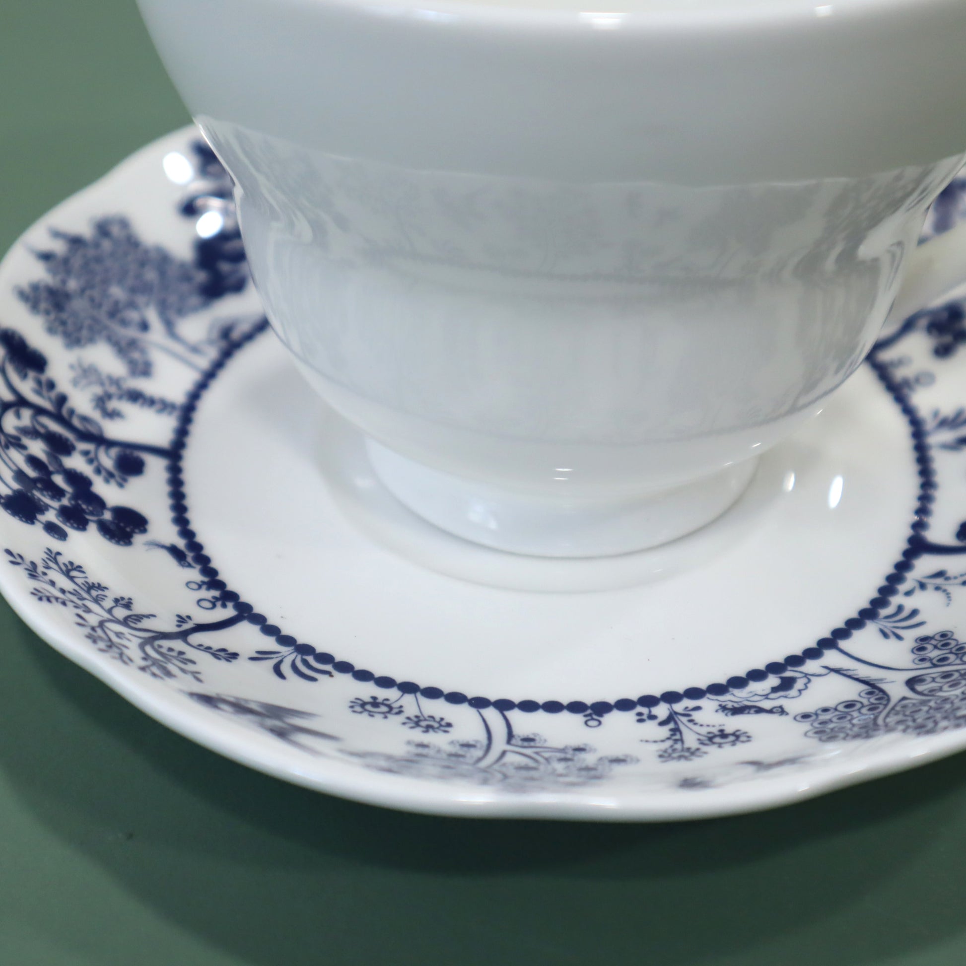 White teacup and saucer with blue floral patterns on a green background