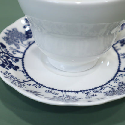 White teacup and saucer with blue floral patterns on a green background