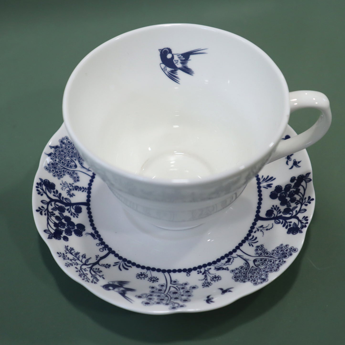 White teacup and saucer with blue floral patterns on a green background