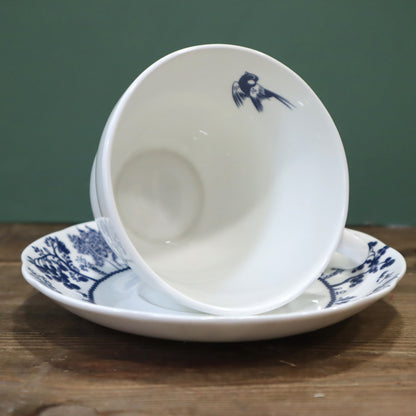 White ceramic bowl with blue floral design on a matching plate against a green background