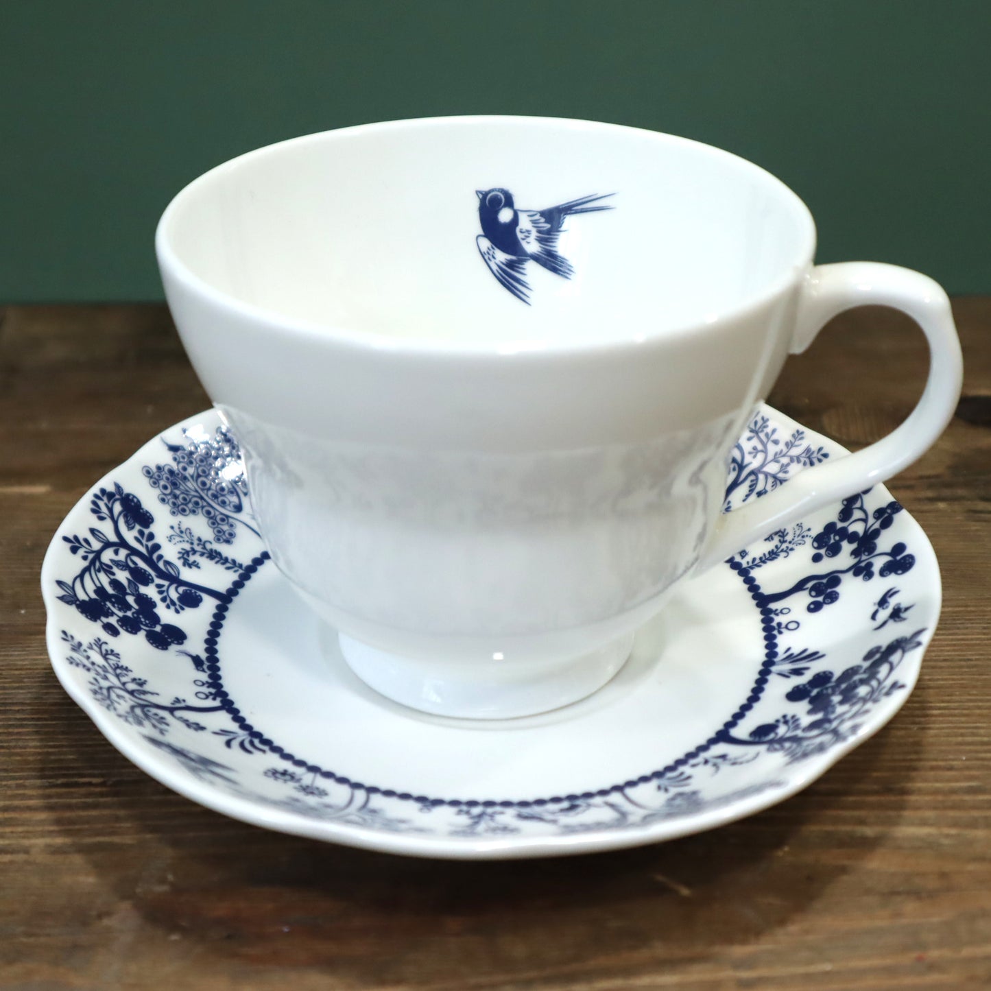 White teacup and saucer with blue floral patterns on a wooden surface.