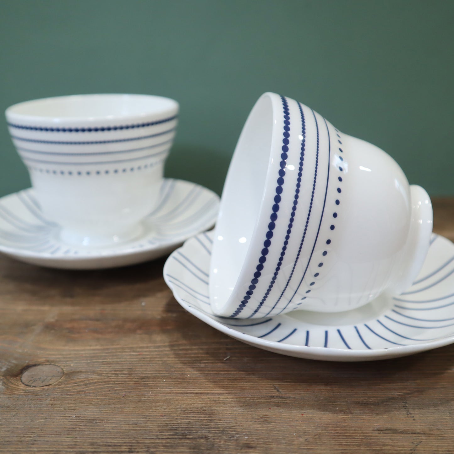 White ceramic cup and saucer with blue stripes on a wooden surface.