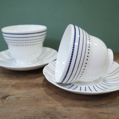 White ceramic cup and saucer with blue stripes on a wooden surface.