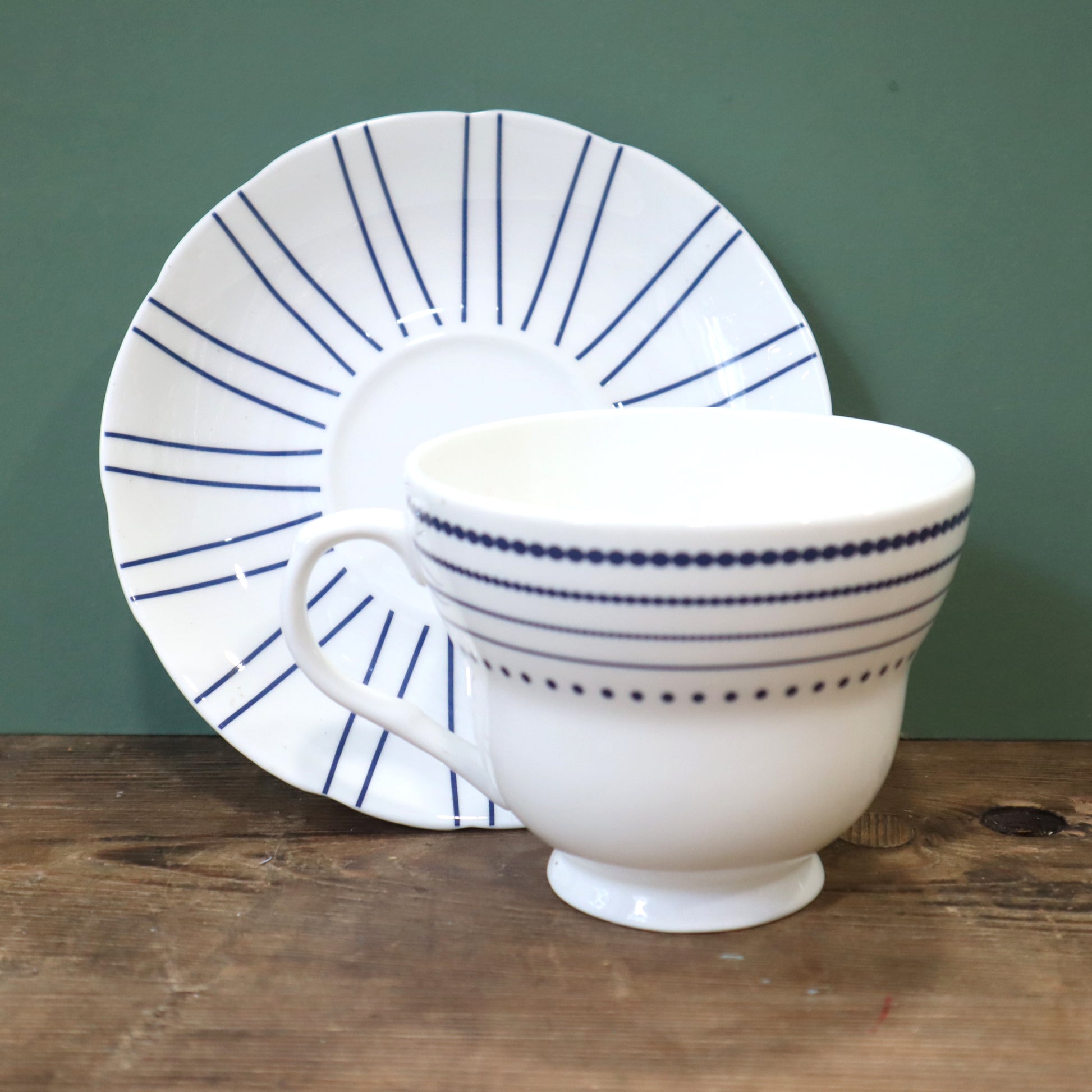 White teacup and saucer with blue stripes on a wooden surface and green background