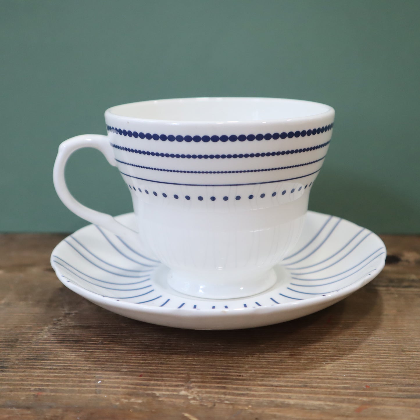 White ceramic cup and saucer with blue stripes on a wooden surface and green background