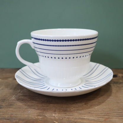 White ceramic cup and saucer with blue stripes on a wooden surface and green background