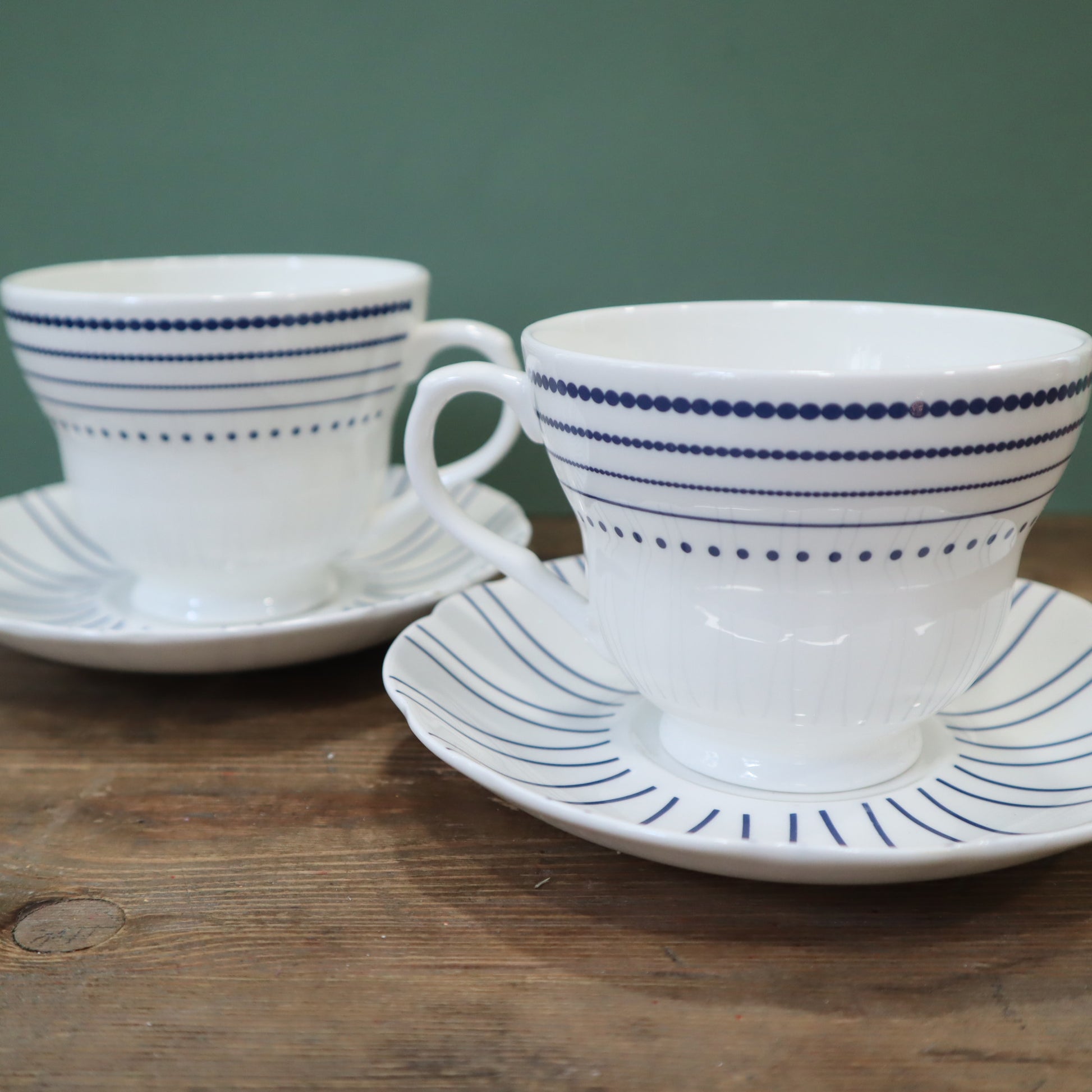 Two white ceramic teacups with blue stripes on saucers against a green background