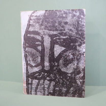 Mixed media artwork with a textured surface featuring a stylized face design on a light green background