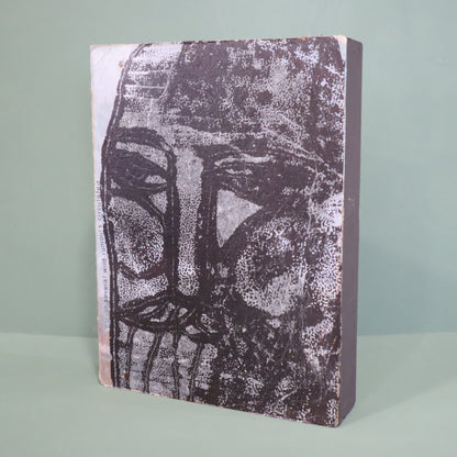 Mixed media artwork with a textured surface featuring a stylized face design on a light green background