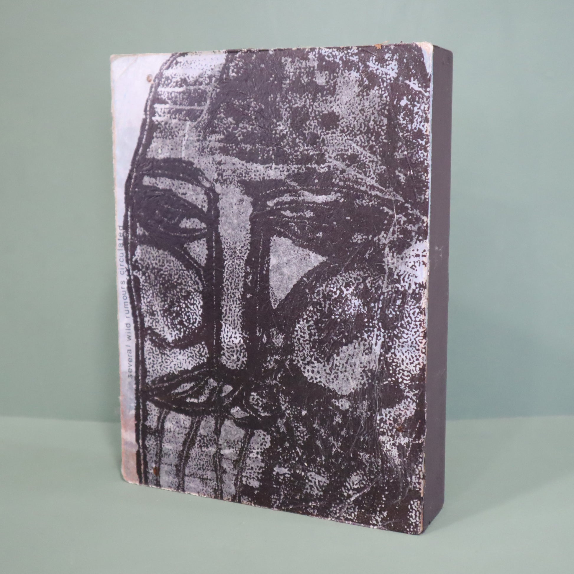 Mixed media artwork with a textured surface featuring a stylized face design on a light green background