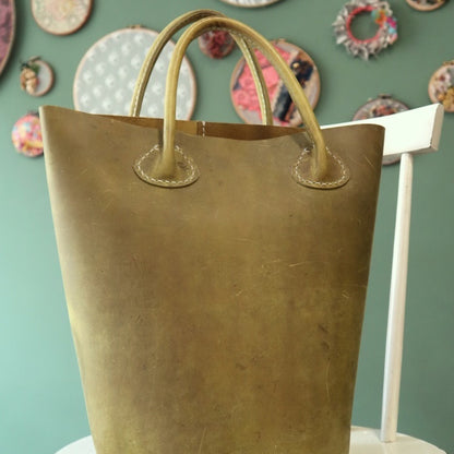 Olive green leather tote bag on a white chair against a green wall.