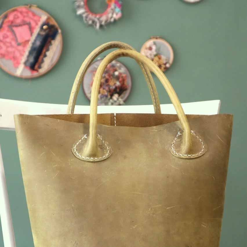 Olive green leather bag with handles against a green wall with decorative plates.