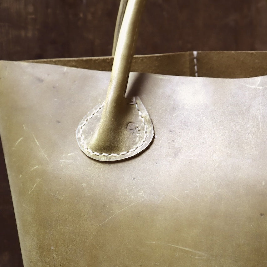 Close-up of a olive green leather bag handle against a wood coloured background