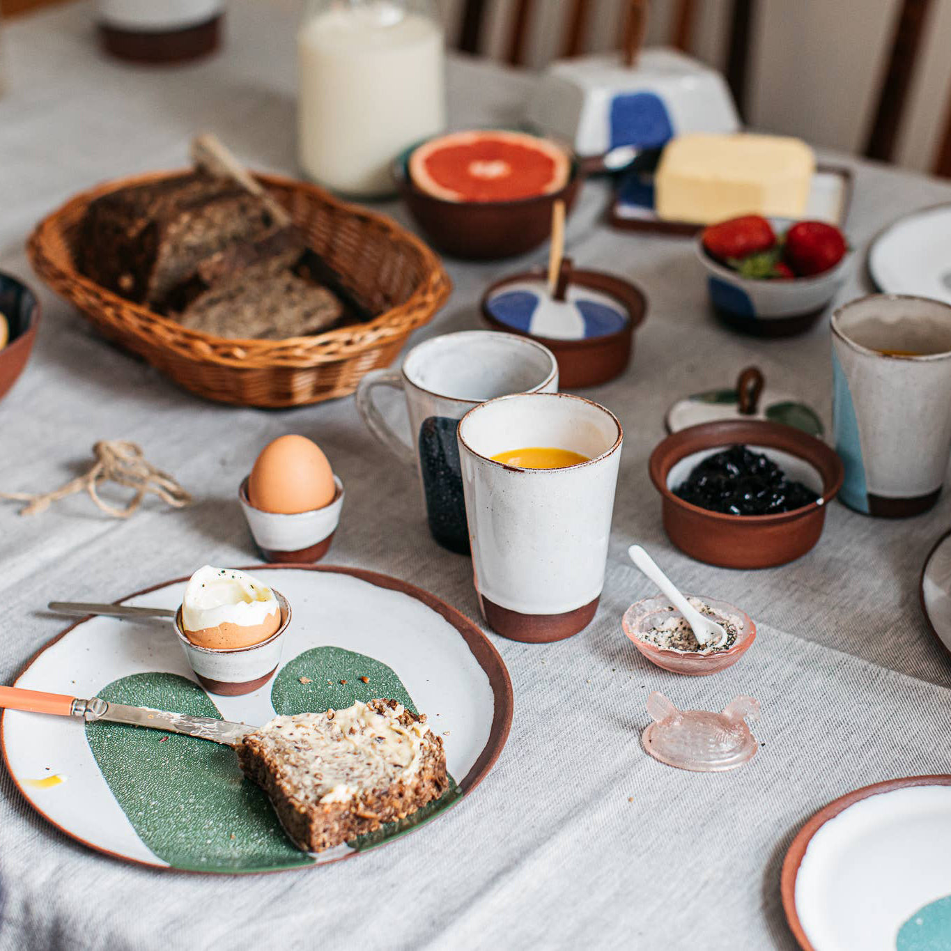 Breakfast table setting with bread, eggs, and coffee on a textured tablecloth.