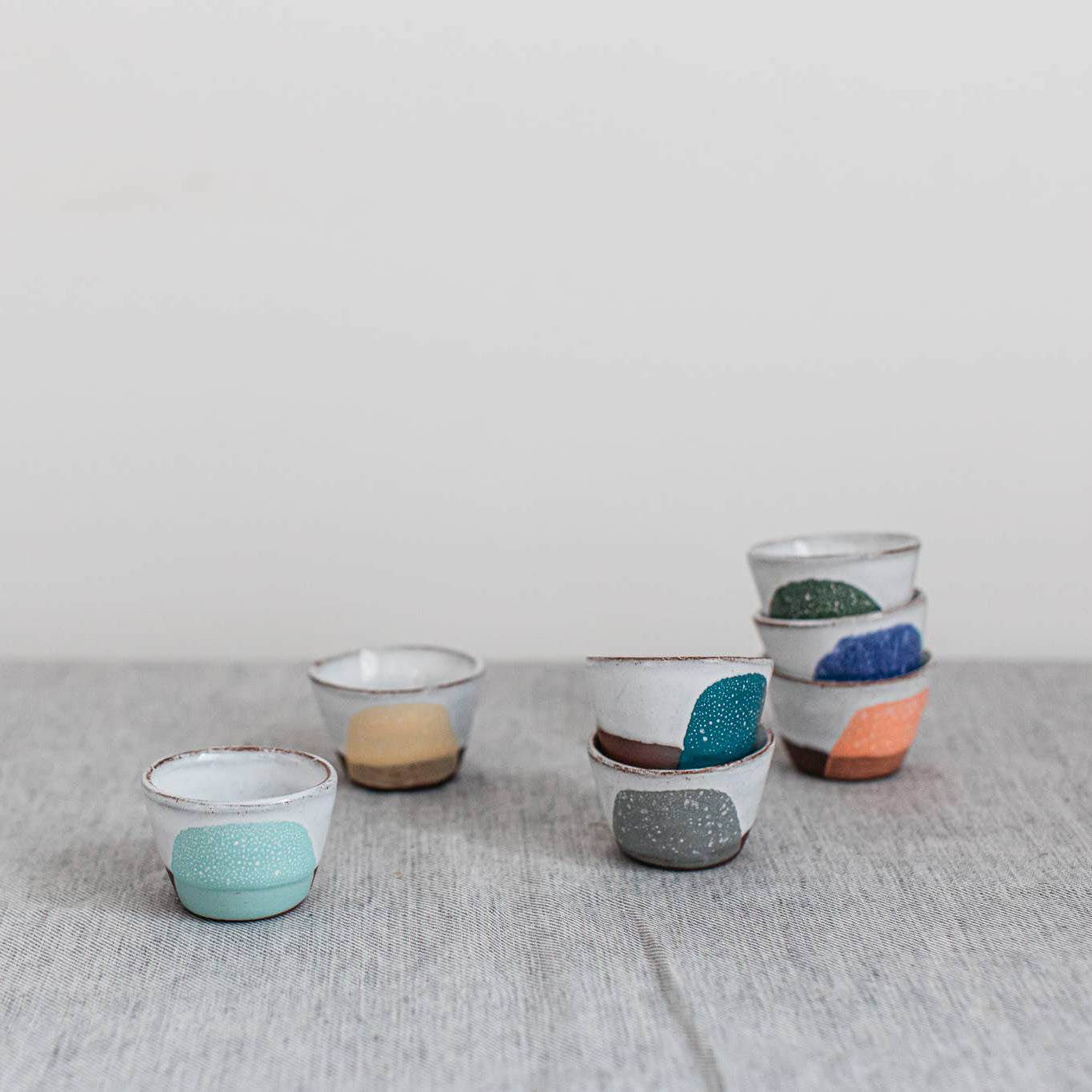 Set of small ceramic egg cups with colorful speckled designs on a textured surface.
