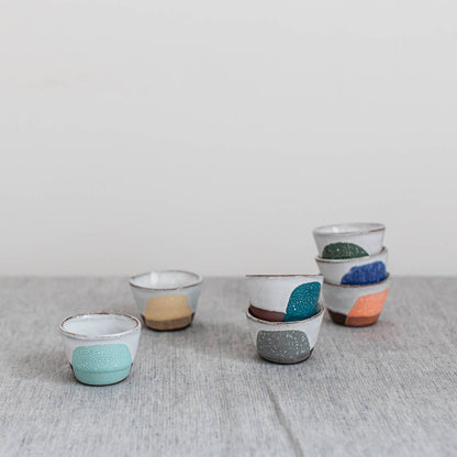 Set of small ceramic egg cups with colorful speckled designs on a textured surface.