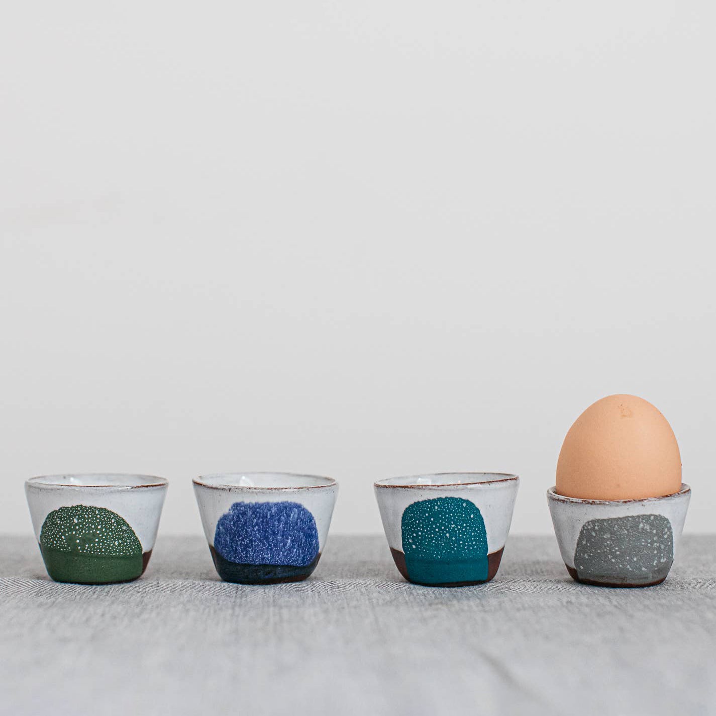 Four ceramic egg cups with different color patterns on a light gray background