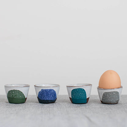 Four ceramic egg cups with different color patterns on a light gray background