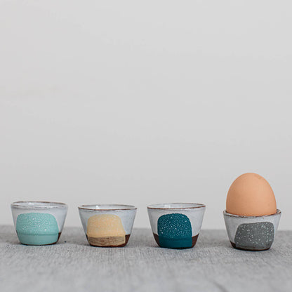 Four ceramic egg holders with speckled patterns on a gray surface.