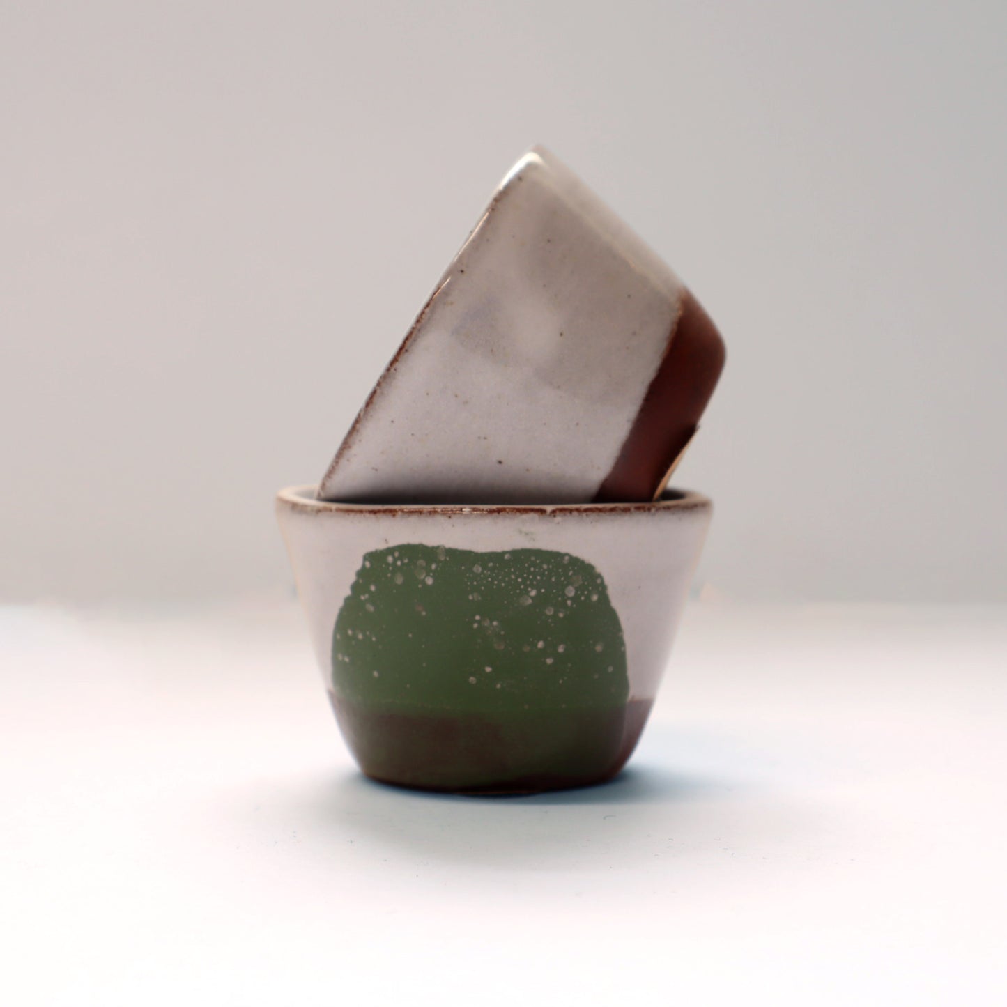 Two ceramic egg cups, one green and one grey, on a light grey background