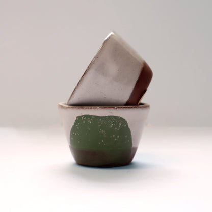 Two ceramic egg cups, one green and one grey, on a light grey background