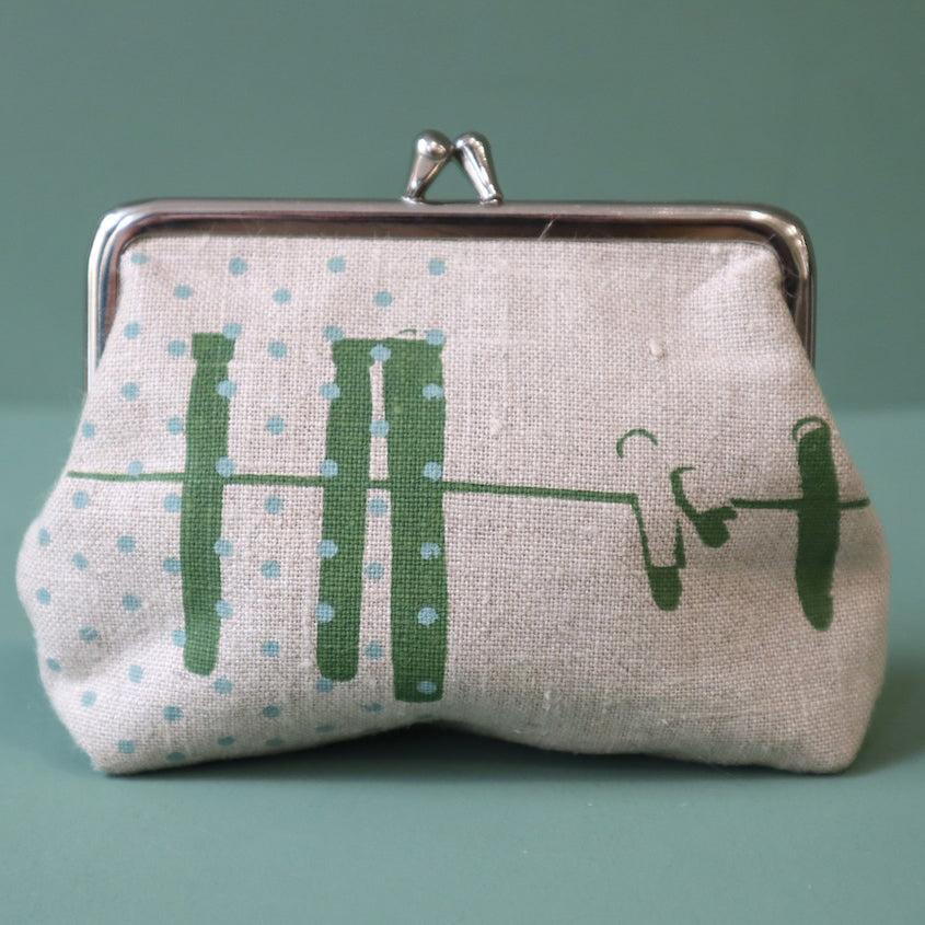 A linen purse with green abstract design of a washing line and blue dots, the purse has a silver clasp to the top