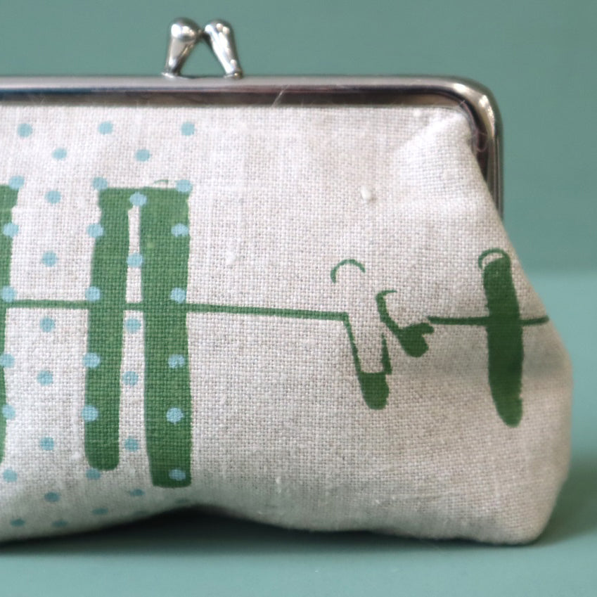 A linen purse with green abstract design of a washing line and blue dots, the purse has a silver clasp to the top