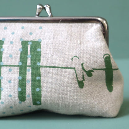 A linen purse with green abstract design of a washing line and blue dots, the purse has a silver clasp to the top