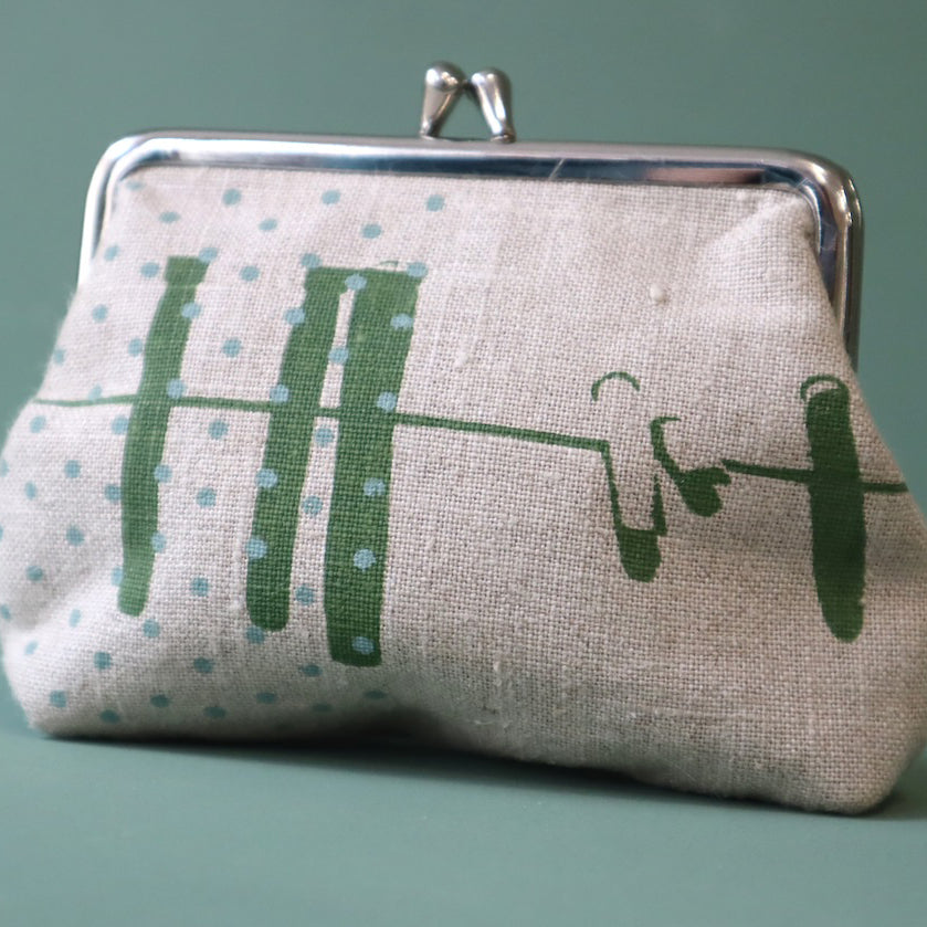 A linen purse with green abstract design of a washing line and blue dots, the purse has a silver clasp to the top