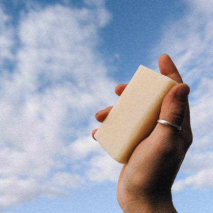 Hand holding a bar of soap to the sky on a slightly cloudy day